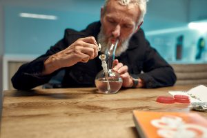 Old man lighting a glass pipe